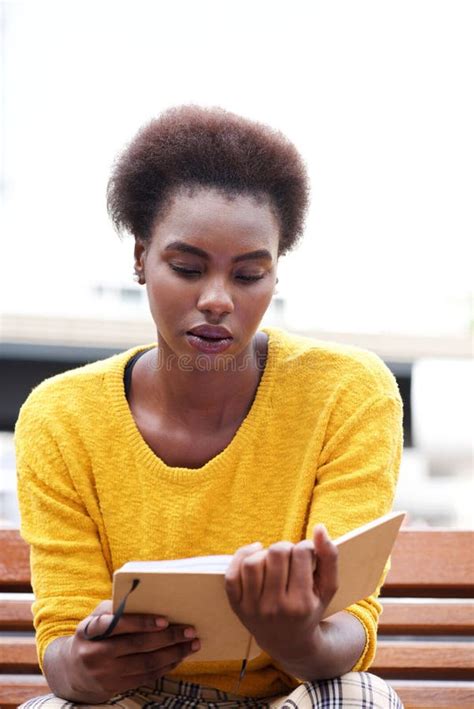 African American Woman Reading Book On Bench Outdoor Stock Photo