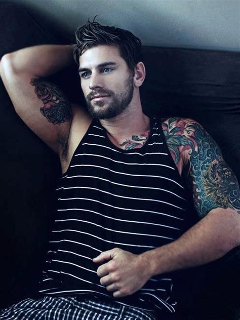 A Man With Tattoos On His Arms And Chest Sitting In A Black Chair Next