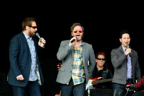 Three Men Singing Into Microphones While Standing Next To Each Other In