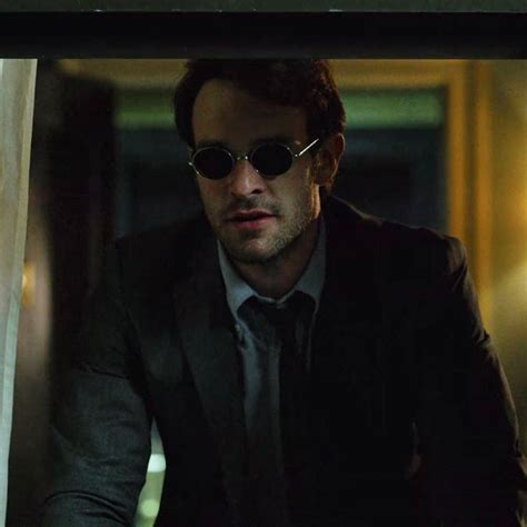 A Man In A Suit And Sunglasses Looking At Something Through A Window With His Hands On His Hips