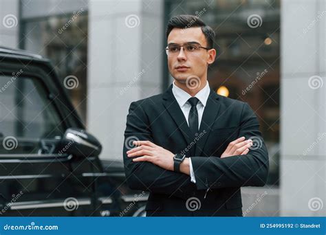 Standing With Arms Crossed Businessman In Black Suit And Tie Is