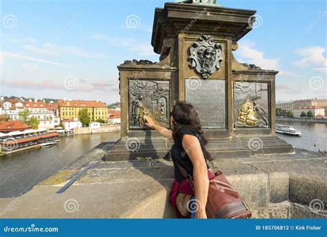 A Tourist Rubs The Bronze Plaque On The Statue Of Saint John Of Nepomuk For Good Luck On The