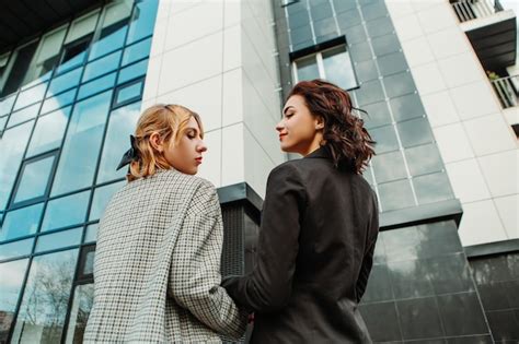 Dos amigas bonitas posando cerca de un edificio de cristal pareja de gay lesbianas niñas