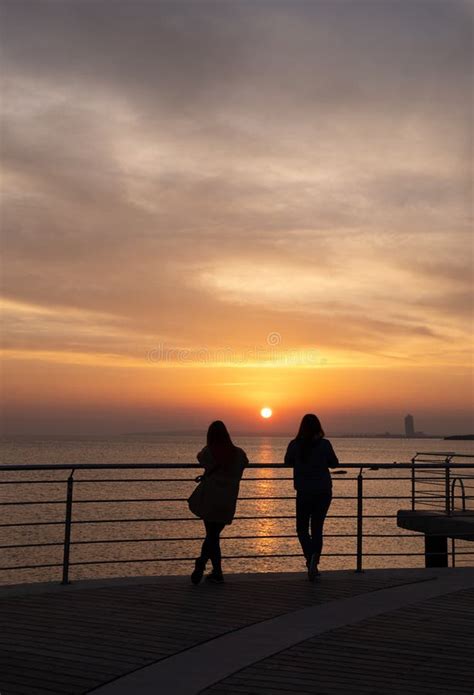 People Standing On A Pier Enjoying Dramatic Orange Sunset At The Sea