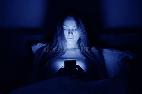 Young Beautiful Woman At Night Sitting In Bed With Smartphone Stock