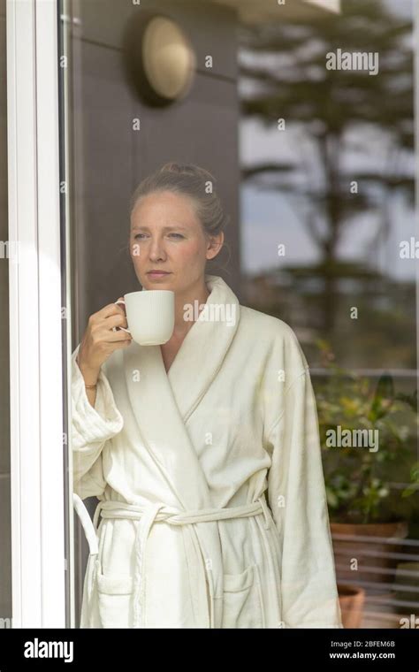 Blonde Woman In Bathrobe Sipping Tea Looking Through Window Stock Photo Alamy