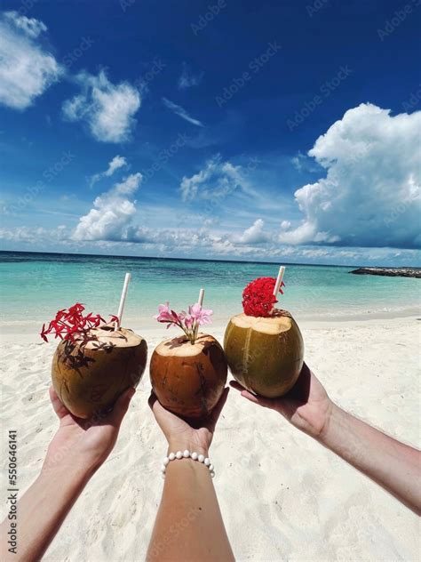 Tropical coconut cocktails in the hands of three people on the beach of ...