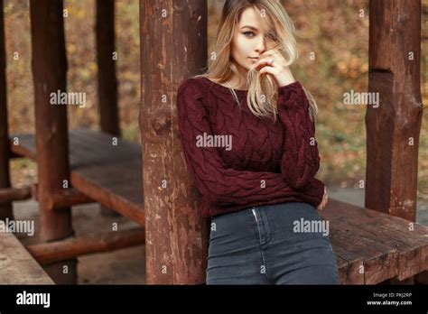 Très belle jeune fille blonde en jeans et chandail tricoté élégant près de piliers en bois Photo