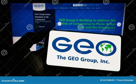 Person Holding Cellphone With Logo Of Us Security Company The Geo Group