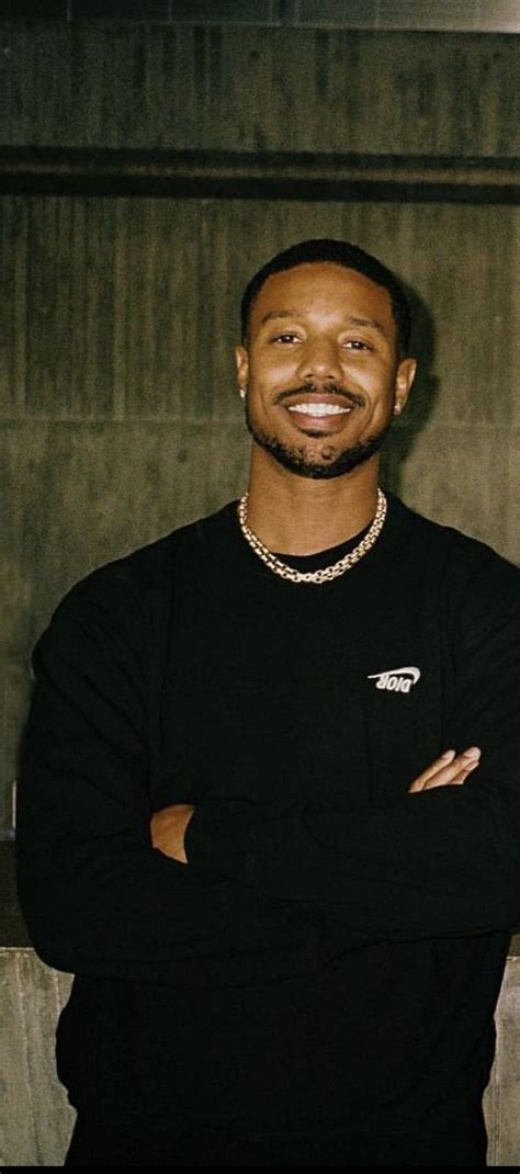 A Man Standing In Front Of A Wall With His Arms Crossed And Smiling At