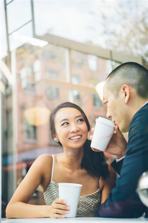 A Man And Woman Sitting At A Table With Coffee Cups In Their Hands Looking Into Each Other S Eyes