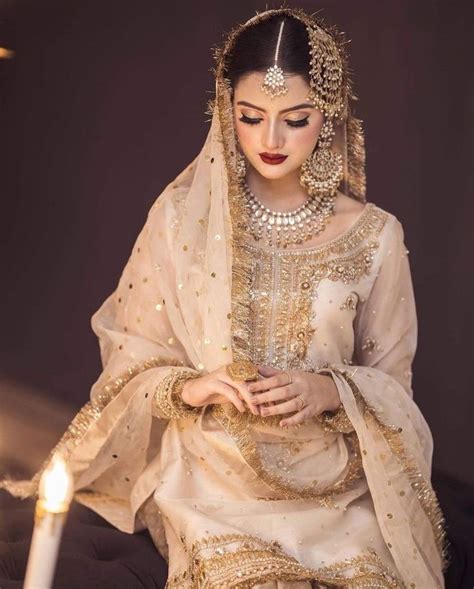 A Woman In A White And Gold Bridal Outfit Sitting On A Bed With A Lit