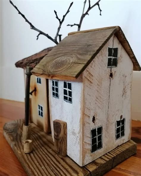 A Small White House Sitting On Top Of A Wooden Table Next To A Bare Tree