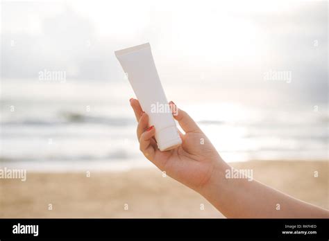 Woman Hand Holding Sunscreen On The Beach With The Sea In Blue Sky