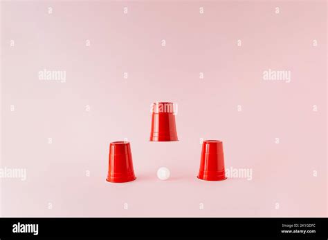 Three Red Plastic Beer Pong Cups With White Ball Under Middle Raised