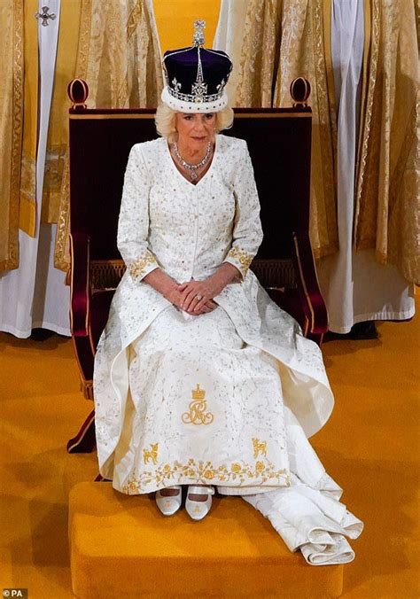 The Queen Is Sitting On A Bench Wearing A White Dress And Tiara With Gold Trim