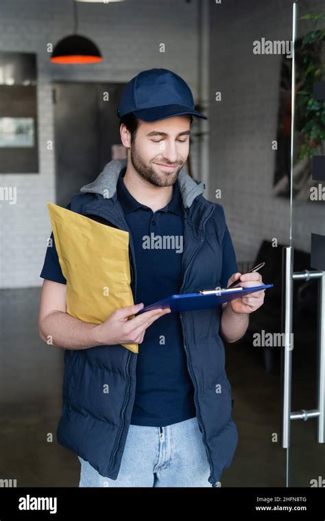 Positive Delivery Man Holding Parcel And Writing On Clipboard In