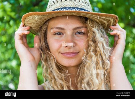 Portrait Of Smiling Blond Woman Wearing Straw Hat Hands On Hat Stock