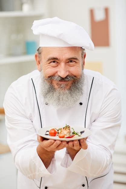 Premium Photo Smiling Senior Chef Presenting Dish