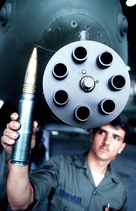 A soldier stands below a GAU-7 Gatling Gun and holds up a 30mm ...