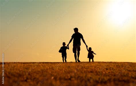 Silhouette Of Father And Children Holding Hands Walking Outdoors In The