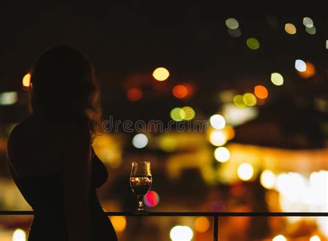 Silhouette Of Naked Woman On The Balcony With A Glass Of Wine On The Background Of A Night City