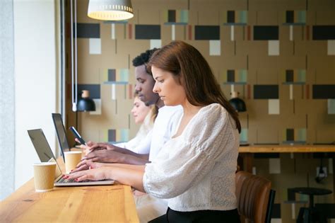 Vista lateral de pessoas trabalhando em laptops e sentadas à mesa perto