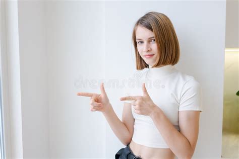 A Young Woman Is Standing In Front White Wall Pointing To The Right