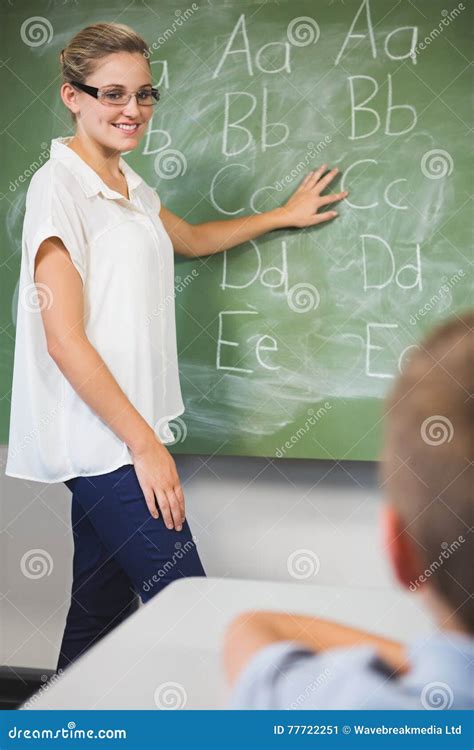 Smiling Teacher Teaching Kids On Chalkboard In Classroom Stock Image