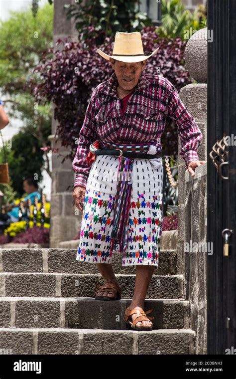 An elderly Mayan man in traditional clothing walks down the stairs in ...