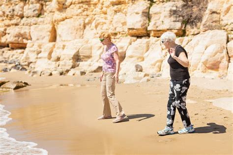 Two Senior Women Walking Along The Rocky Seashore And Playing With The