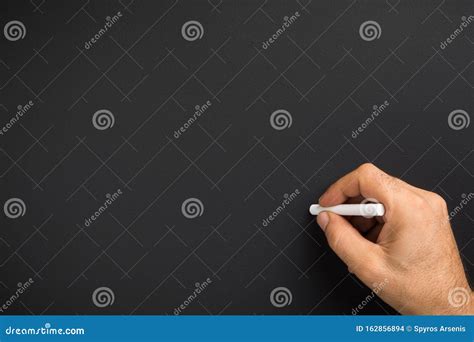 Close Up Of Man Hand Holding Chalk Against Blank Black Chalkboard Stock