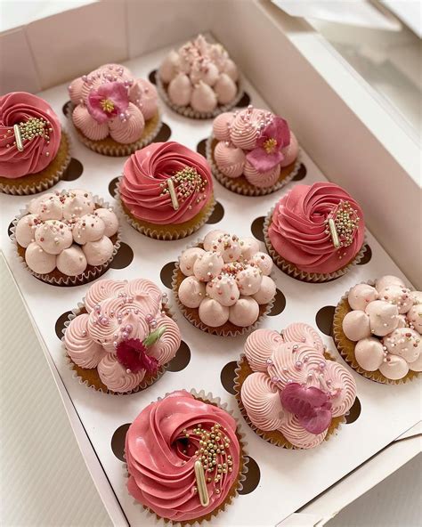 Twelve Cupcakes With Pink Frosting And Flowers In A White Box On A Table