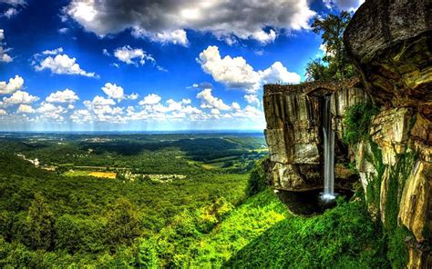 Brown Rugged Cliff With Waterfalls And Green Dense Forest Under White