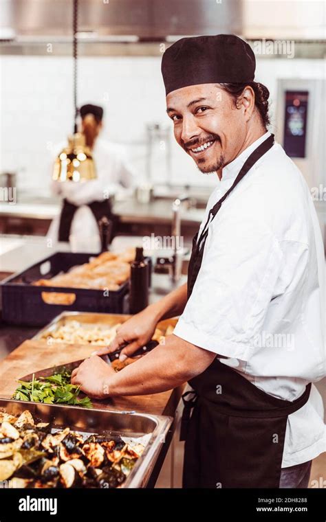 Side View Portrait Of Happy Male Chef Cutting Leafy Vegetables At