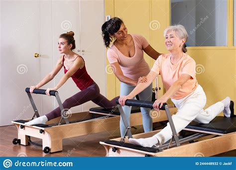 Aged Woman Doing Pilates On Reformer With Hispanic Female Trainer Stock