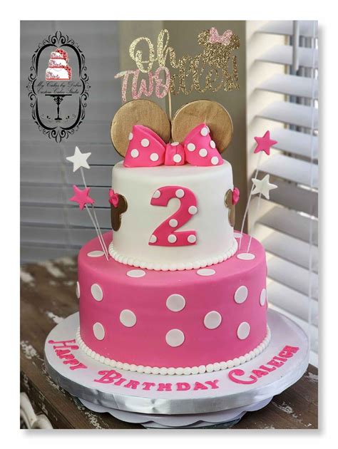 A Pink And White Birthday Cake With Minnie Mouse Topper On It S Side