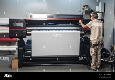 Technician worker operator works on large premium industrial printer and plotter machine in ...