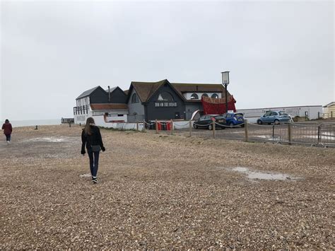 a woman walking on the beach towards some buildings and cars parked in ...