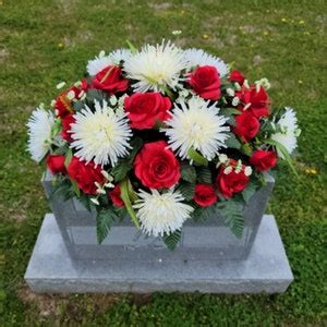 A Headstone Saddle With Red Roses And Cream Mum Grave Flowers For