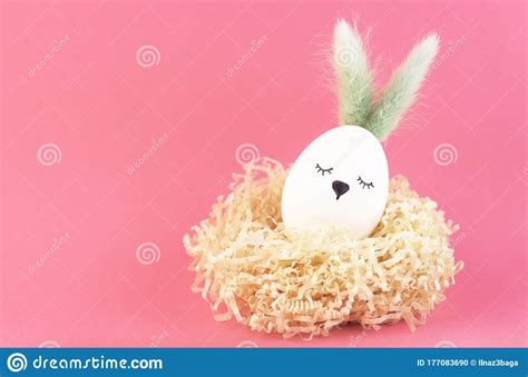 Un Huevo Blanco De Pascua Con Orejas Y Una Cara Linda En Un Nido Rosa