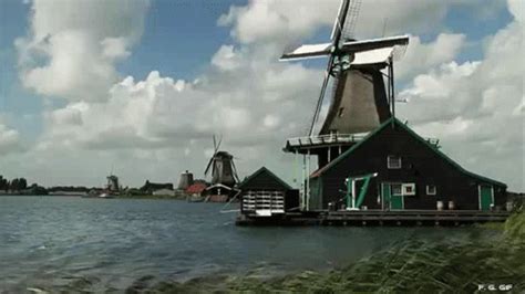 A Windmill Sitting On Top Of A Body Of Water Next To A Lush Green Field