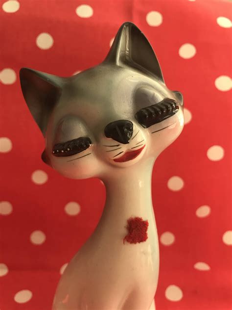 A Cat Figurine With Red Spots On Its Face And Eyes Sitting In Front Of A Polka Dot Background