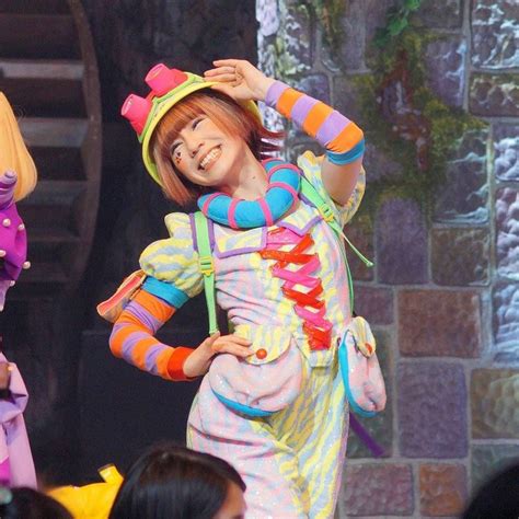 Two Dolls Dressed As Clowns On Stage With People In The Back Ground Watching Them