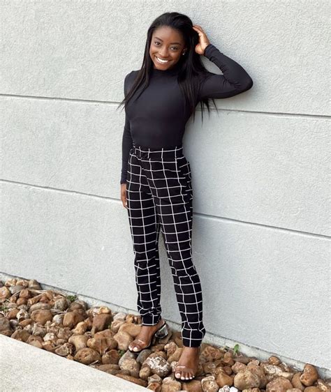 a woman leaning against a wall with her hand on her head and smiling at the camera