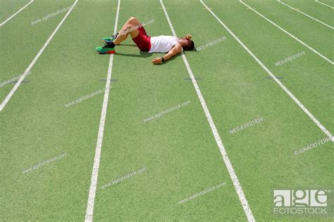 Tired Athlete Lying On Running Track At Sports Field Stock Photo