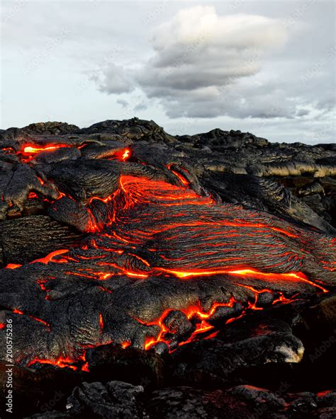 A lava flow emerges from an earth column and flows in a black volcanic landscape, in the sky ...