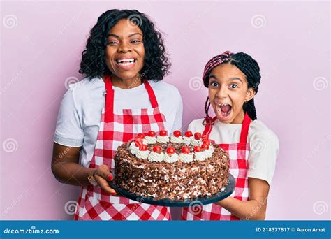 Beautiful African American Mother And Daughter Wearing Baker Apron Holding Homemade Cake