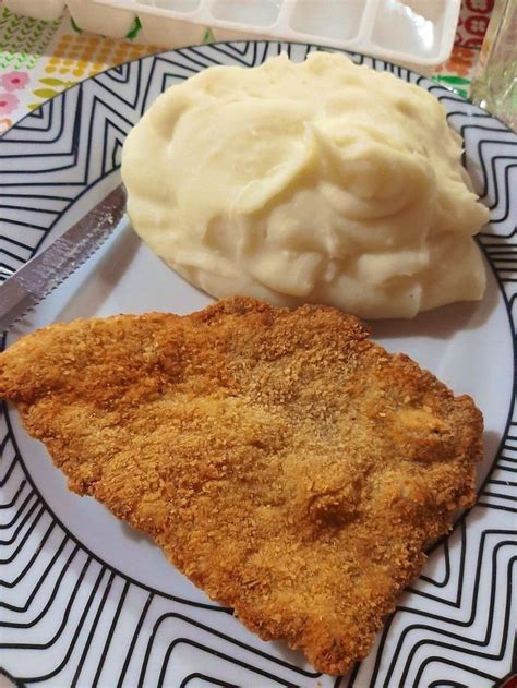 A White Plate Topped With Two Pieces Of Fried Chicken Next To Mashed