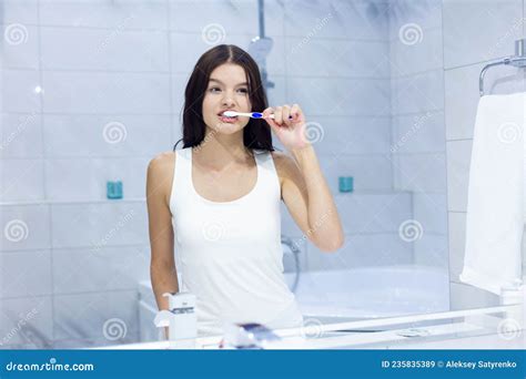 Front View Portrait Of Pretty Young Female Brushing Her Teeth In Front